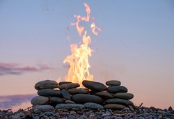 the fire burning in the stone place on the pebbly beach in the evening sky