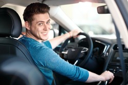 Happy young driver behind the wheel inside new car. Lifestyle scene in the car dealership