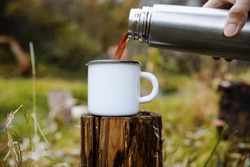 Person pours hot tea from a thermos into a mug. Cropping, close-up. Concept for outdoor activities, hot drink, hike, travel.