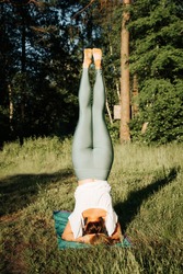 Slim athletic young woman practicing yoga asana, headstand. Rear view of a girl standing on her head on a yoga mat outdoors. Healthy active lifestyle. Vertical image.