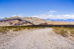Travelling on an unpaved road through a remote area of Death Valley National Park; mountains and blue sky in the background; California