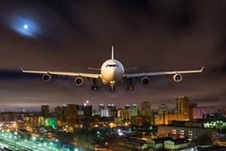 White passenger plane in flight during the night. Aircraft flying in moonlight over the night city. Airplane front view.