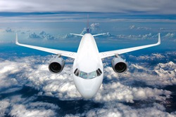 White passenger jet plane in the blue sky.  Aircraft flying high above the mountains. Airplane front view.