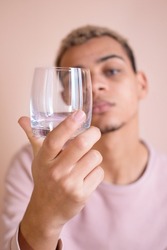 Empty glass in hand; defocused conceptual portrait of young African American man on pink background