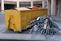 Huge heap on metal Big Overloaded dumpster waste container filled with construction waste, drywall and other rubble near a construction site.