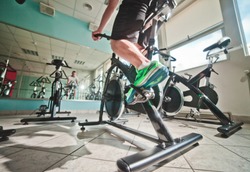 Wide angle view of man in sports sneakers and shorts does exercises on cardio bike at spinning class. Healthy lifestyle concept