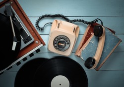 Vinyl player, rotary phone, vinyl plates, old books. Old-fashioned objects on a blue wooden background. Retro style, 70s. Top view.