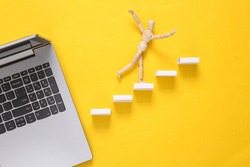 Career growth, business concept. Wooden puppet climbing up the steps and laptop on yellow background 