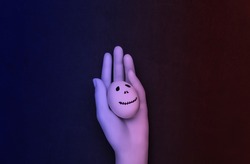 Halloween theme. Mannequin hand holding egg with hand drawn scary ghost face in neon light