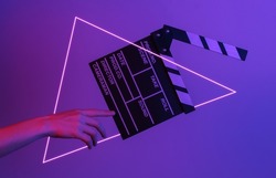 Hand touches film clapper board in neon light with triangle. Cinema industry, entertainment. Concept art, minimalism