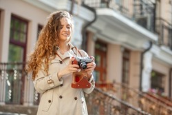 Beautiful curly-haired Caucasian woman with a retro camera in the city. Tourism concept