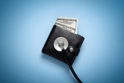 Wallet with money and a stethoscope on a blue background. Business concept