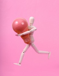Wooden puppet holding pink light bulb on pink background
