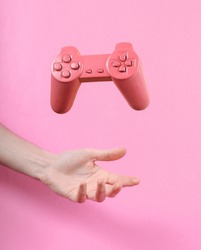 Hand and Levitating pink gamepad on pink background. Minimalistic still life. Concept art. Video game