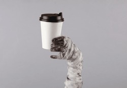 Mummy hand holding coffee cup isolated on gray background. Halloween concept