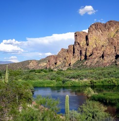 View of a high desert landscape beneath a blue sky with white clouds from across the Salt River in the Salt River Recreation Area; Tonto National Forest in Arizona
