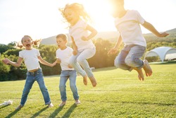 A group of children have fun playing in nature. Children jump over the rope. Warm summer evening with sunset light.