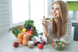 Woman on a diet. Young and happy woman eating healthy salad sitting on the table with green fresh ingredients indoors. High quality photo
