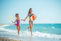 Children at sea play merrily. Two sisters run, jump on the beach in summer. High quality photo.