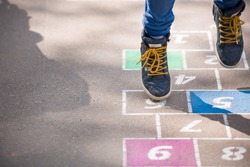 Closeup of boy's legs and hopscotch drawn on asphalt. Child playing hopscotch on playground outdoors on a sunny day. outdoor activities for children. 
