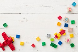 Top view on wooden cubes with numbers and colorful toy bricks and  plane on white wooden background. Toys in the table