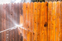Stay at Home house repairs , Pressure Washing Fence with a high pressure washer , cleaning old dirty planks of wood on Wooden Fence in Suburb Neighborhood