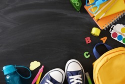 Dive into the world of education. Top view flat lay of educational tools, schoolbag, pair of shoes, water bottle, colorful letters on blackboard background with empty space for promo or text