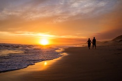 Couple walking and holding hands silhouette with orange sunset on the beach.