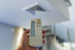 Man or woman Adult  used remote control for turn on- off air condition. Hand holding remote in front of blurred air condition vent square type on ceiling. Close up selective focus.
