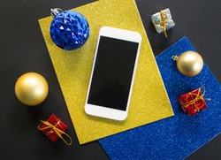 Christmas tree ornament and smartphone flat composition. White smartphone with black screen on table. Christmas or New Year mockup with personal gadget. Smartphone template with winter holiday decor