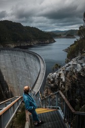 Young girl standing on massive Gordon dam water reservoir in Tasmania, admiring, looking to distance