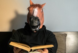 Funny scene with a man with a horse mask trying to read a book and learn