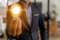 Man holding a light bulb with orange light, Portrait of a business man in a suit standing holding a light bulb. Business ideas. Male businessman background image and business growth.