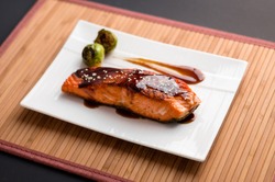 Teriyaki salmon plate on bamboo mat. Japanese cuisine inspired dinner consisting of a grilled salmon fillet glazed in delicious teriyaki sauce (soy sauce base). Healthy brussel sprouts as sides.