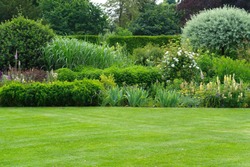 Scenic Summertime View of a Beautiful English Style Landscape Garden with a Green Mowed Lawn, Leafy Trees and Colourful Flower Bed