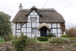 Exterior view of an old thatched cottage house on a street in an English village