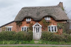 Exterior view and front door of a beautiful old thatched cottage house on a street in an English town
