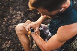 Young athletic man using fitness tracker or smart watch before run training outdoors. Close-up photo with dark background.