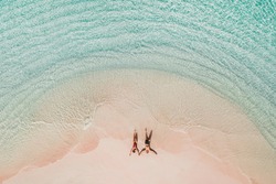 Couple lying on famous pink beach in Komodo national park. Turquoise mint color clear water, tropical vacations on honeymoon. Drone aerial view from above.