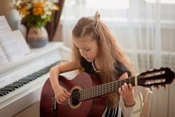Home lesson on music for a girl with a guitar and piano. The idea of activities for the child at home during quarantine