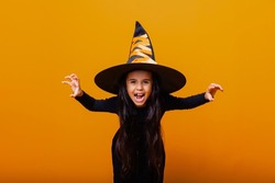 Portrait of an angry little girl in a witch costume, on a yellow background. halloween.