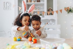 Little African American boy and girl paint Easter eggs at home. black children are preparing for Easter.