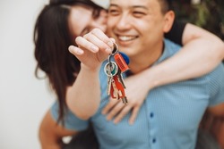 A happy married couple celebrates moving to a new house, shows the keys, stands in an apartment, the concept of a mortgage on real estate.keys close-up
