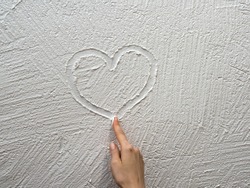 Finger paints a heart on a white stucco wall.