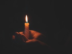 Burning candle in male hand on a black background. 