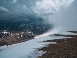 Wonderful dramatic landscape with big snowy mountain peaks above low clouds. Snow storm on top of a mountain. Atmospheric large snow mountain tops in cloudy sky.