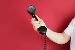 male hand holds a telephone receiver Handset from vintage apparatus on red background, concept of anonymous psychological assistance, helpline number, modern communication technology, call center