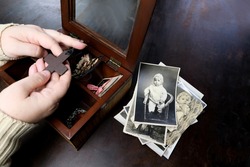 female hands sorting dear to heart memorabilia in old wooden box, stack of retro photographs, wooden cross, vintage photographs of 1960, concept of family tree, genealogy, childhood memories
