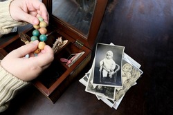 female hands are sorting dear to heart memorabilia in an old wooden box, a stack of retro photos, a wooden rosary, vintage photographs of 1960, concept of family tree, genealogy, childhood memories