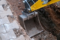 excavator bucket digs earth in trench on street, concept of repairing urban communications, conducting electrical networks to buildings, underground laying optical fiber for communication